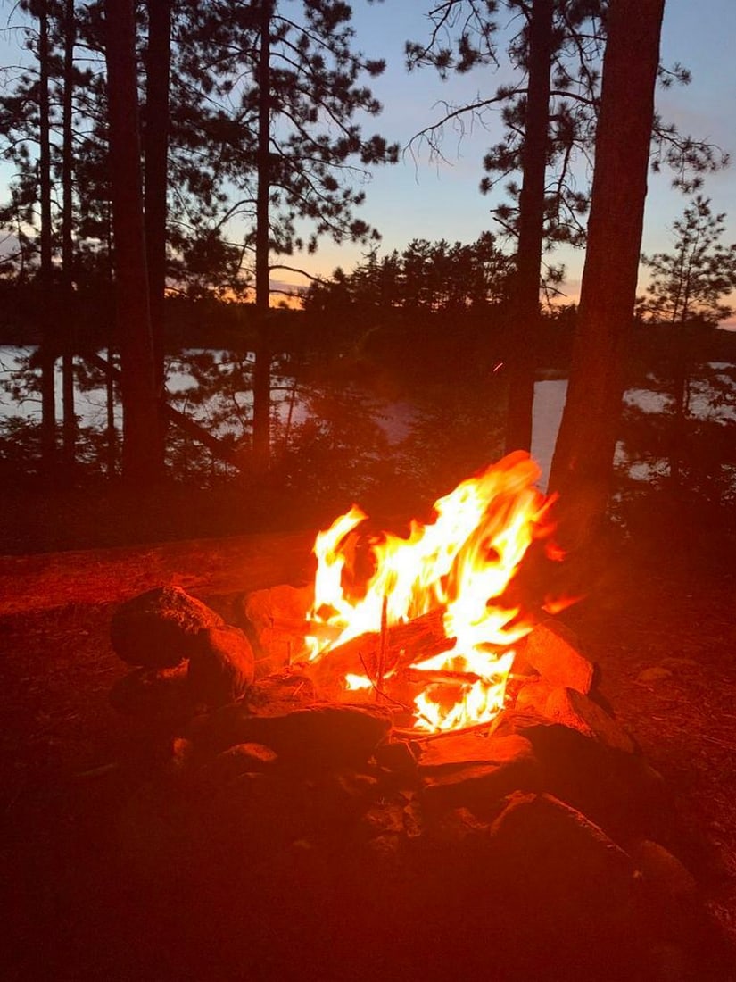 Campfire Glow: Campfire Glow Experience the cozy charm of an evening in the wilderness with this exclusive hand-painted canvas opportunity. The photograph captures a fire burning warmly in a campsite firepit, while 