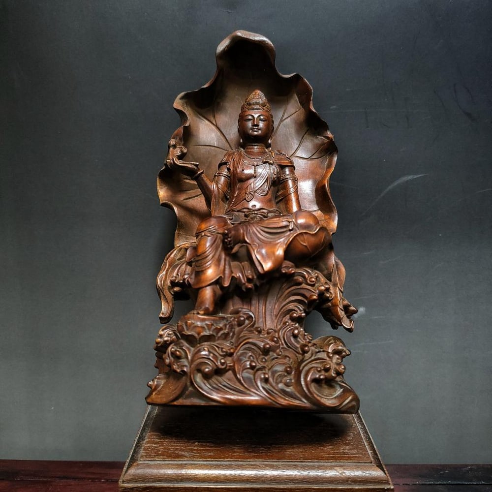 Wood Carved Guanyin Buddha Statue: Wood Carved Guanyin Buddha Statue This beautiful wood carving showcases the Guanyin Buddha seated in peaceful repose on a throne, the back of which is intricately shaped like a large, sacred leaf, a