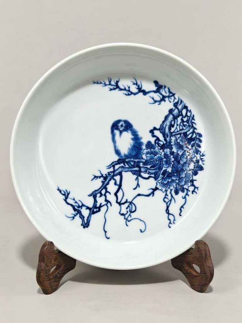 Blue and White Porcelain Plate: Blue and White Porcelain Plate This elegant blue and white porcelain plate features a serene scene of a bird perched delicately on a flowering branch, rendered with timeless grace. The intricate