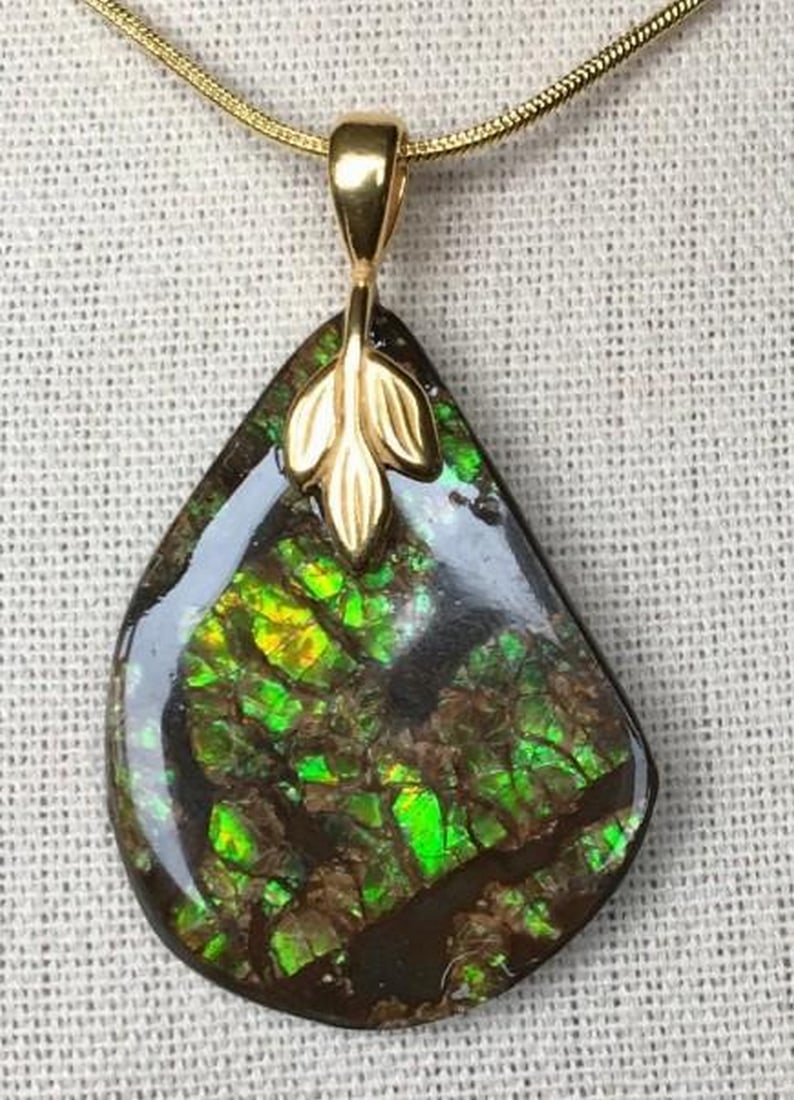 Eclipse Glow Ammolite Pendant: Eclipse Glow Ammolite Pendant This is an ammolite pendant that has a stone with green gem along with a bit of gold. The cab has areas with no gem, but this actually gives the cab a bit of a dramatic