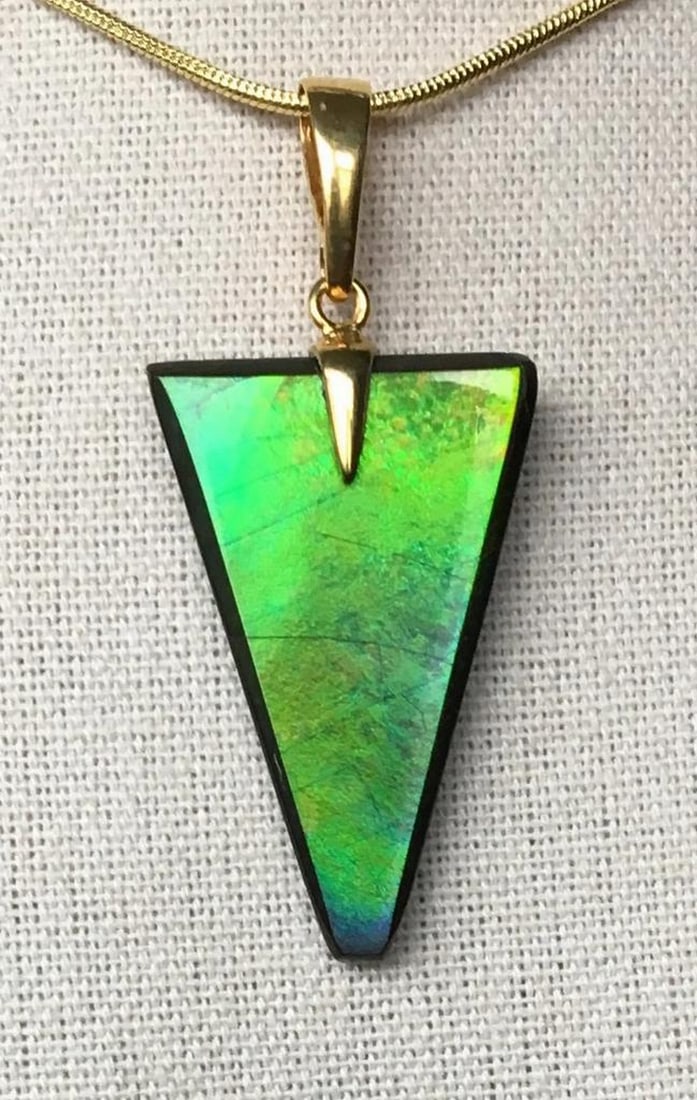 Prism Ammolite Necklace Pendant: Prism Ammolite Necklace Pendant This ammolite pendant showcases a beautifully cut designer gemstone, exuding elegance. The gem features a rich green hue with subtle gold and blue overtones, enhanced