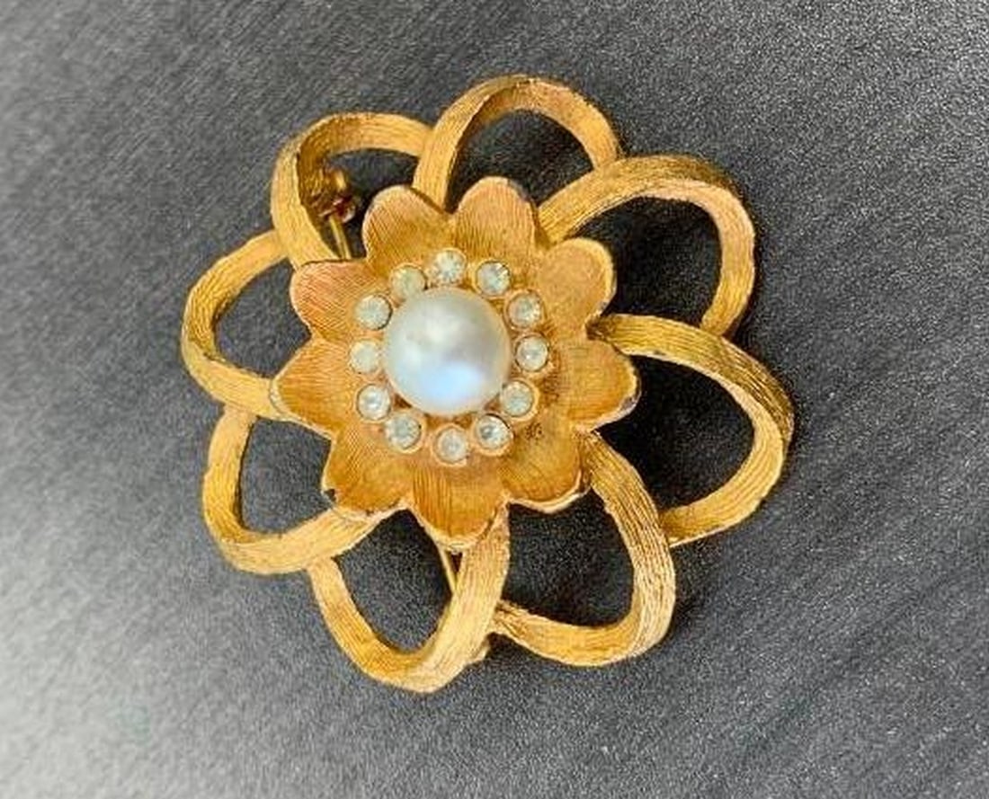 Gold-Tone Floral Brooch with Pearl Center: Gold-Tone Floral Brooch with Pearl Center This elegant flower-shaped brooch features a luminous central pearl encircled by a ring of sparkling gemstones, creating a radiant focal point. The layered