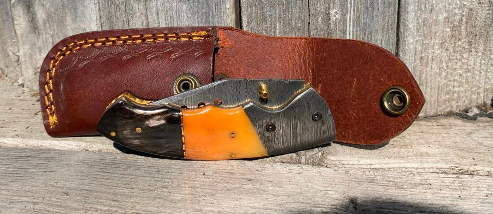 The Phantoms Pain Folding Damascus Knife: The Phantoms Pain Folding Damascus Knife This pocket knife features a sleek and practical design with a subtle touch of orange. The handle sports a muted orange hue, offering just a hint of color whil
