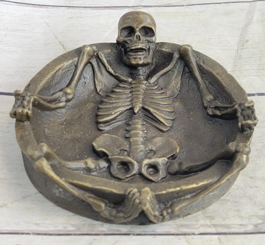 Skeleton Bronze Ashtray Sculpture in the Style of Milo - 5'' x 1.5'': Skeleton Bronze Ashtray Sculpture in the Style of Milo - 5" x 1.5" This bronze sculpture presents a skeletal figure emerging from an ashtray form, with its legs draped over the edge. The piece h