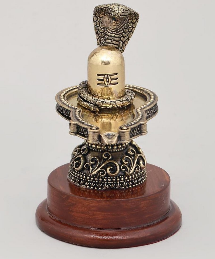5" Brass Shiva Lingam with Vasuki Serpent on Wooden Base: 5" Brass Shiva Lingam with Vasuki Serpent on Wooden Base This 5" brass statue depicts the Shiva Lingam, symbolizing the limitless creative and transformative power of Lord Shiva, with the prot
