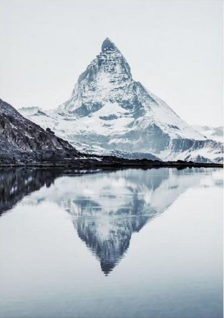 Alpine Reflection Canvas Print: Alpine Reflection Canvas Print An artwork showing a snow-capped mountain peak reflected in calm light blue water. The scene has a quiet and open atmosphere with clear, simple detail. The work is