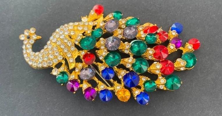 Radiant Gemstone Peacock Brooch: Radiant Gemstone Peacock Brooch A dazzling peacock brooch adorned with a vibrant array of colorful gemstones that shimmer across its elegantly detailed body. The head is crowned with brilliant silver 
