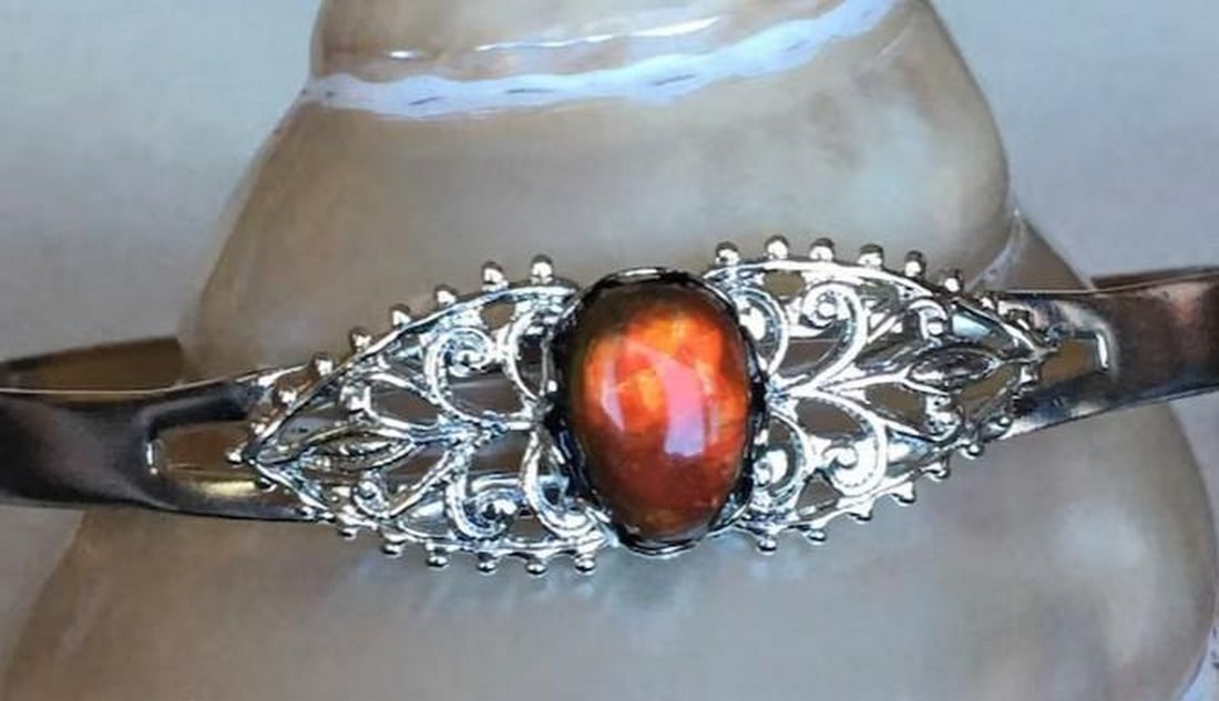 Scarlet Blaze Ammolite Cuff Bracelet: Scarlet Blaze Ammolite Cuff Bracelet The Scarlet Blaze Ammolite Cuff Bracelet is a bold statement of fiery elegance. Featuring a striking red ammolite gemstone, its vibrant hues shimmer with every mov