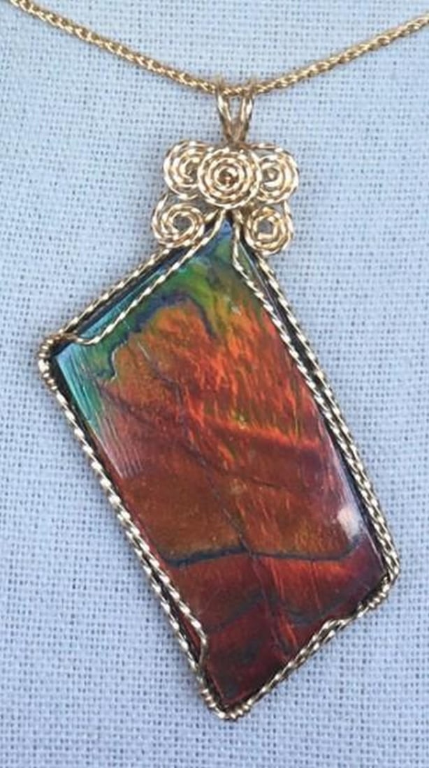 Eternal Ember Ammolite Pendant: Eternal Ember Ammolite Pendant This ammolite pendant captivates with a fiery display of red, green, and orange hues, shimmering with every movement. The gemstone, formed over millions of years from