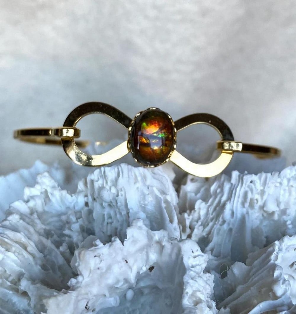 Aurora Essence Ammolite Cuff: Aurora Essence Ammolite Cuff This cuff bracelet features a freeform ammolite gemstone, approximately 10mm x 8mm, set in a gold-plated base metal. Designed for comfort, it sits well on a slender wrist 