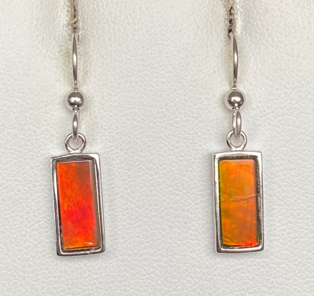 Reddish Orange Ammolite Earrings: Reddish Orange Ammolite Earrings These earrings feature 12mm x 5mm low-dome quartz-capped triplets in sterling silver settings with an anti-tarnish rhodium finish. Suspended from matching