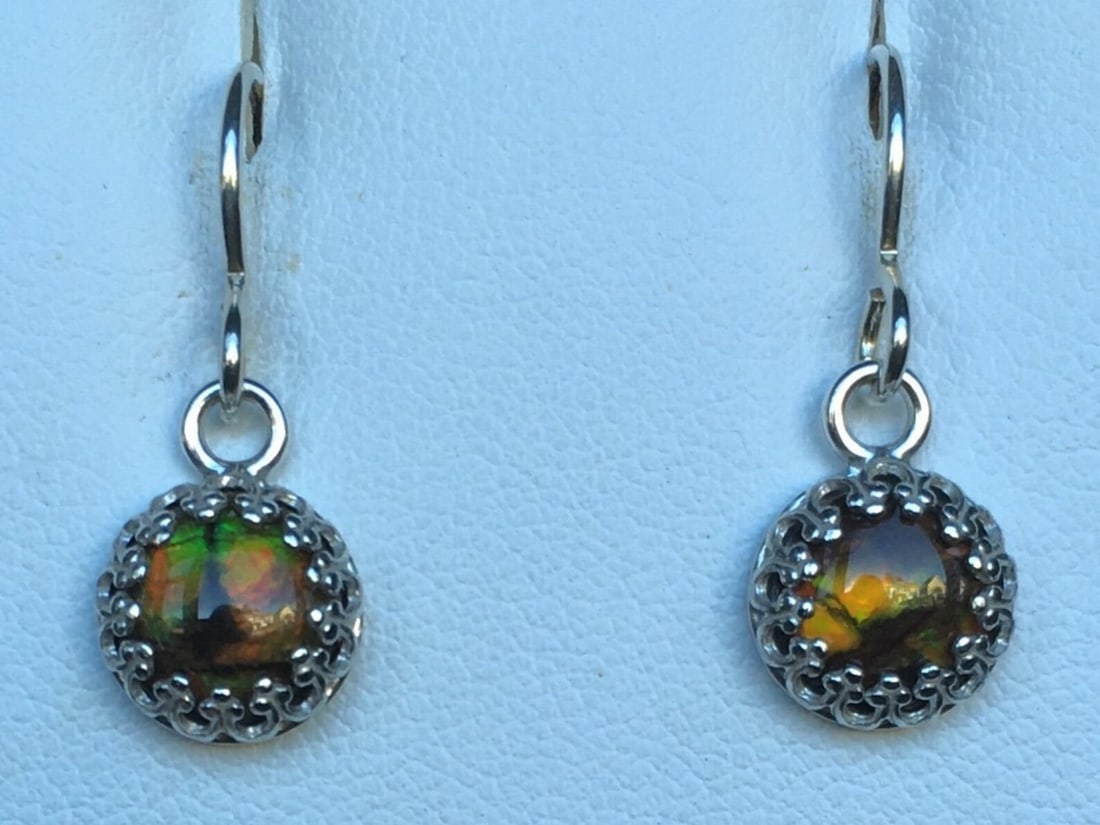 Ammolite Cab Earrings: Ammolite Cab Earrings These earrings feature 6mm round gemstones, elegantly set in sterling silver gallery wire and suspended from French hooks for a timeless look. Dimensions: Diameter 6mm View photo