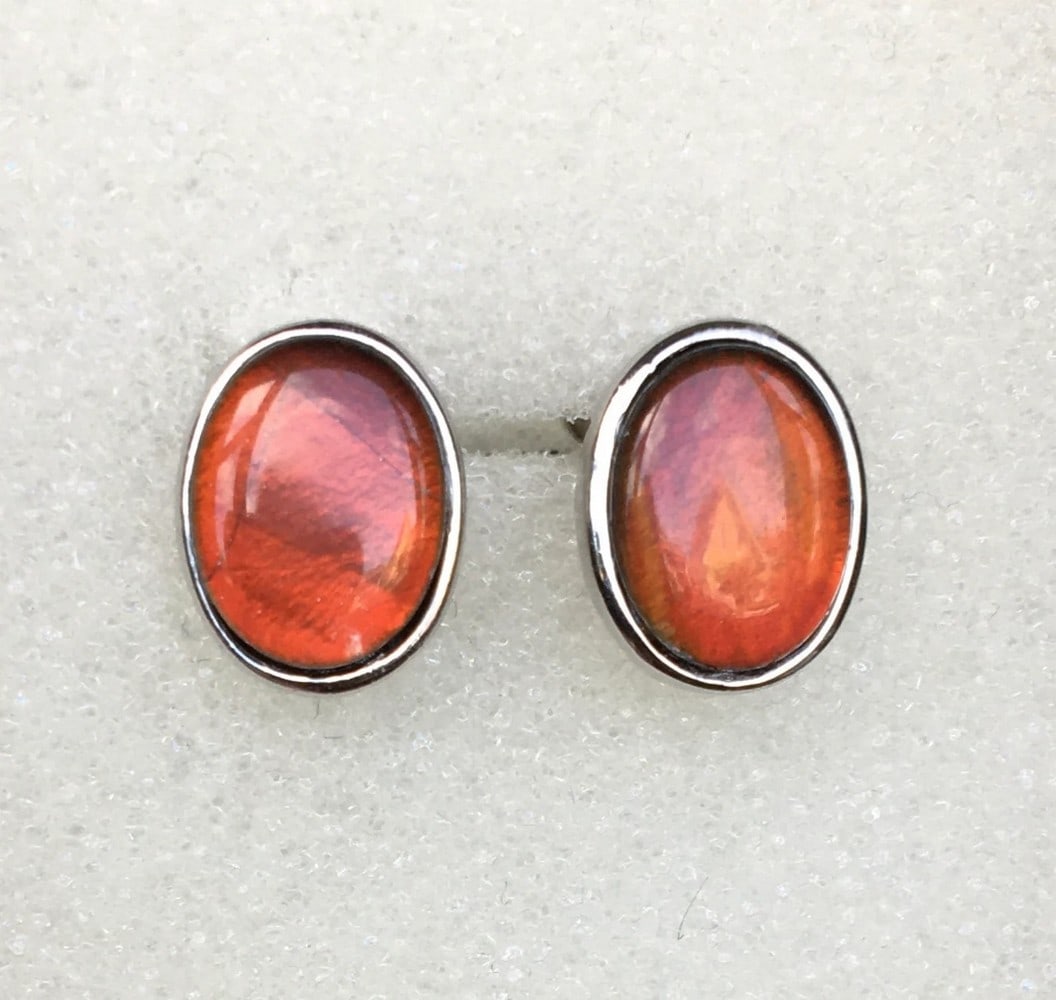 Autum Orange Ammolite Stud Earrings: Autum Orange Ammolite Stud Earrings This pair of Ammolite stud earrings features 9mm x 7mm low-dome red triplets that shift to green at extreme angles. Set in rhodium-plated sterling silver bezels, th