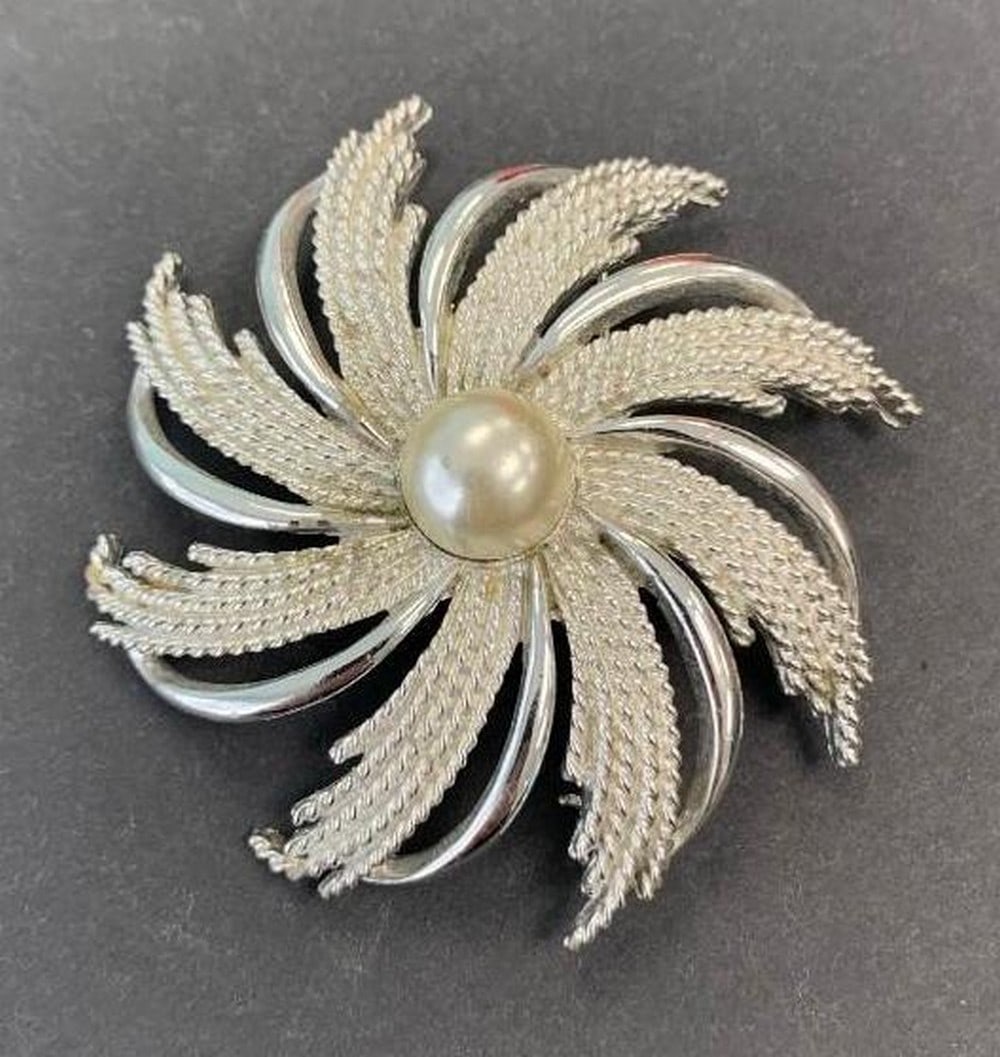 Floral Brooch with Center Pearl: Floral Brooch with Center Pearl This elegant brooch features a luminous pearl at its center, framed by a beautifully sculpted silver-colored floral design. Delicate and timeless, it adds a touch of