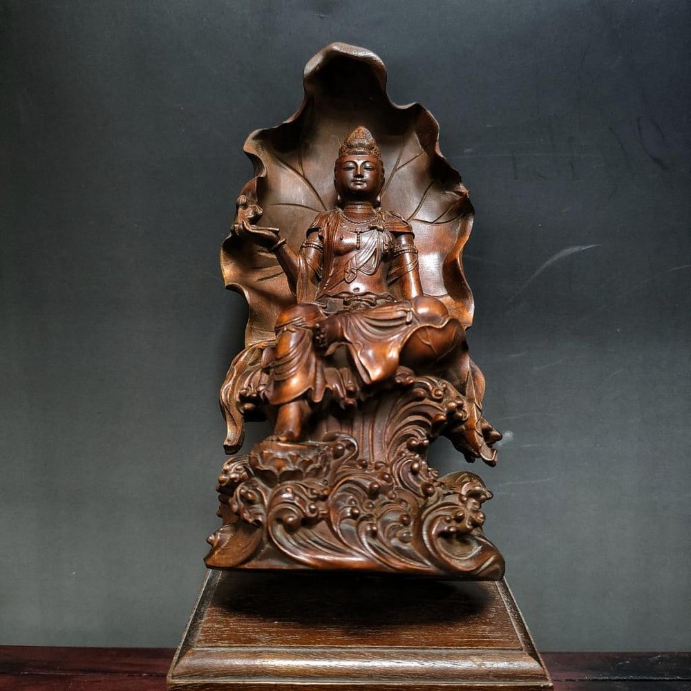 Wood Carved Guanyin Buddha Statue: Wood Carved Guanyin Buddha Statue This beautiful wood carving showcases the Guanyin Buddha seated in peaceful repose on a throne, the back of which is intricately shaped like a large, sacred leaf, a