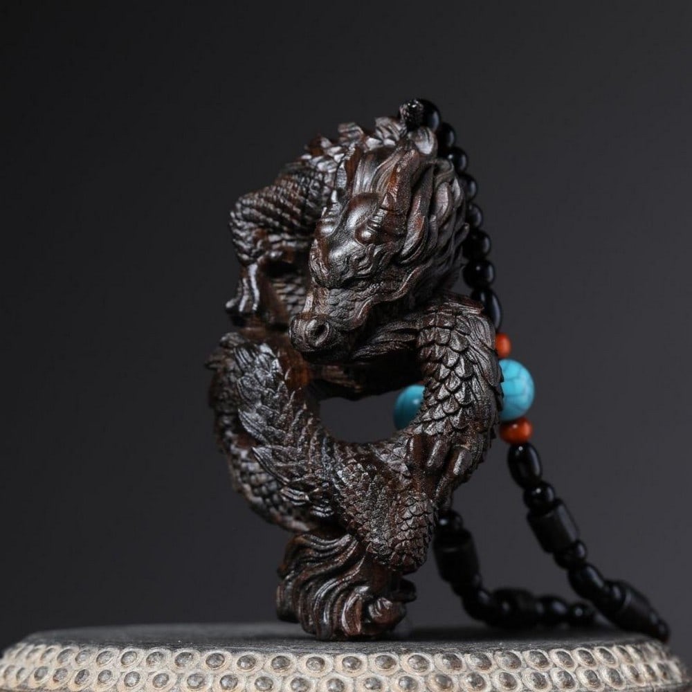 Agarwood Chinese Dragon Pendant: Agarwood Chinese Dragon Pendant This exquisite agarwood pendant features an intricate hollow carving of a Chinese dragon, masterfully sculpted to showcase both the natural beauty of the wood and the m