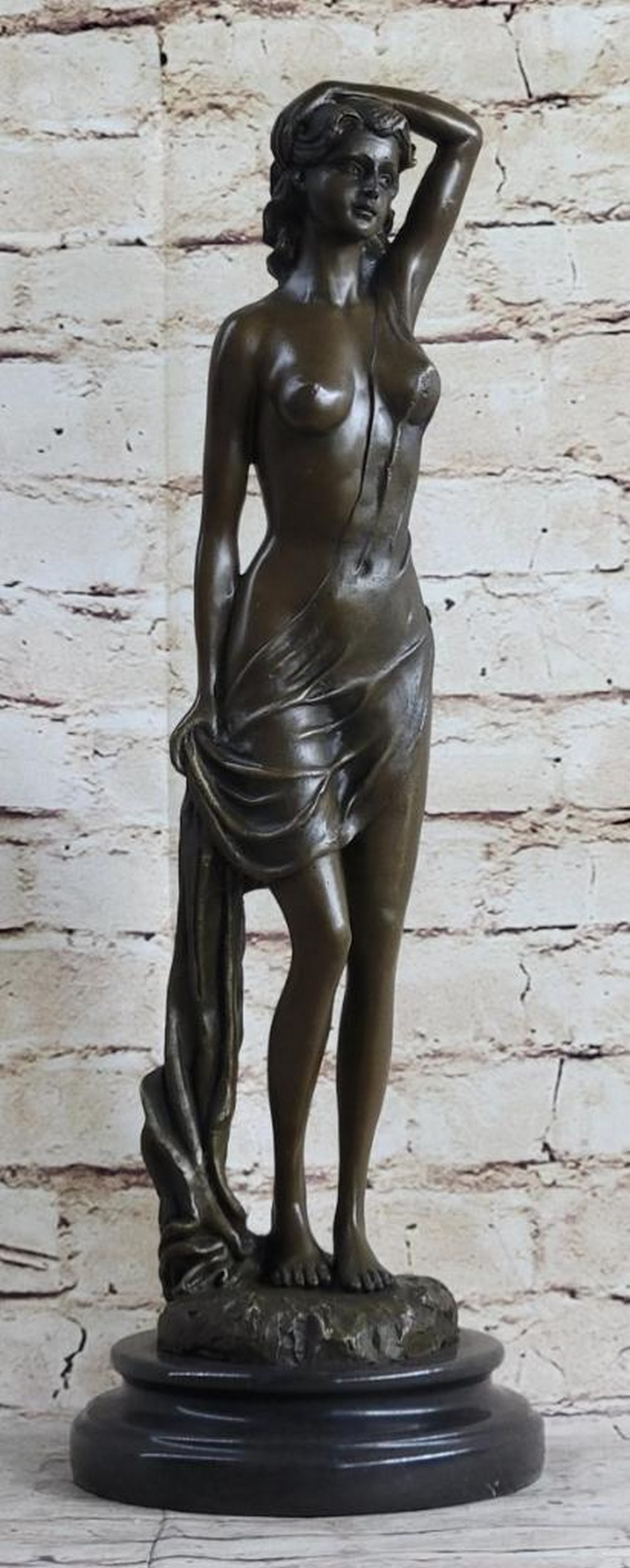 Nude Female Bronze Sculpture by Jean Patoue – 18" x 6": Nude Female Bronze Sculpture by Jean Patoue – 18" x 6" An elegant bronze sculpture of a nude female figure, standing in a relaxed yet poised posture with one arm raised and the other gently 