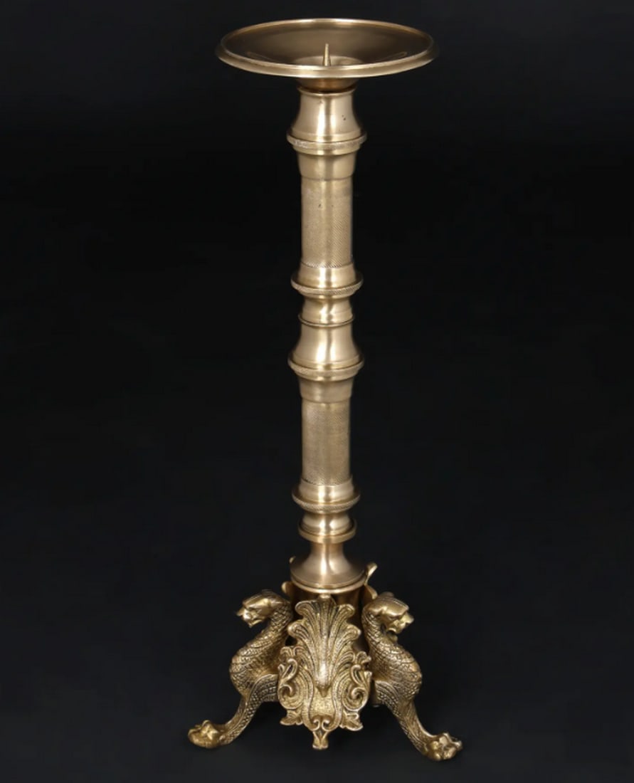 Brass Candle Stand with Griffin Design – 19": Brass Candle Stand with Griffin Design – 19" A 19-inch brass candle stand featuring a griffin-inspired design. The structure incorporates classical motifs and mythological elements, with a verti