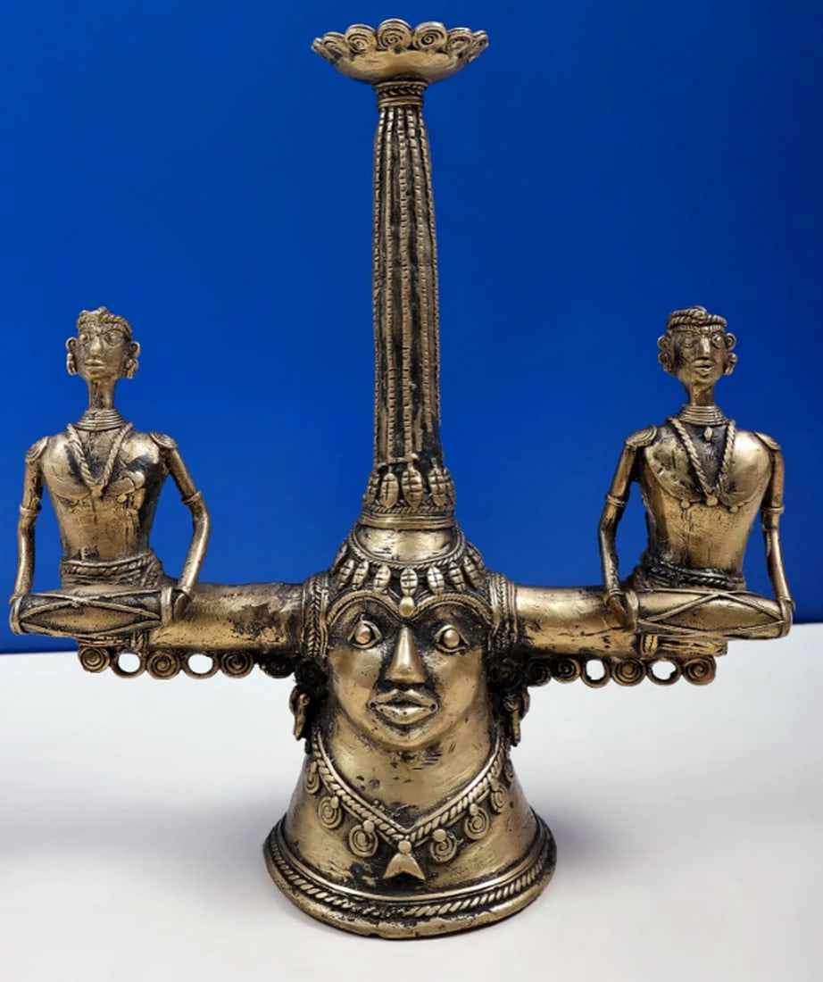 12" Tribal Brass Candle Stand: 12" Tribal Brass Candle Stand Handmade in brass, this candle stand reflects the Dhokra style, crafted using the traditional lost-wax casting method. The design features a lotus atop a straight