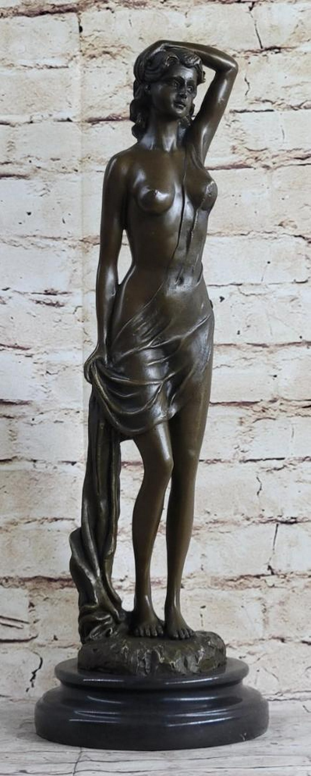 Nude Female Bronze Sculpture by Jean Patoue - 18'' x 6'': Nude Female Bronze Sculpture by Jean Patoue - 18" x 6" An elegant bronze sculpture of a nude female figure, standing in a relaxed yet poised posture with one arm raised and the other gently cl