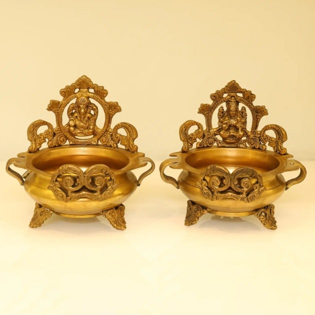 6.5'' Ganesha Lakshmi Urli (Pair): 6.5" Ganesha Lakshmi Urli (Pair) Crafted from brass, this pair of Urlis features the divine forms of Lord Ganesha and Goddess Lakshmi. The bowls are designed for traditional use, often filled with