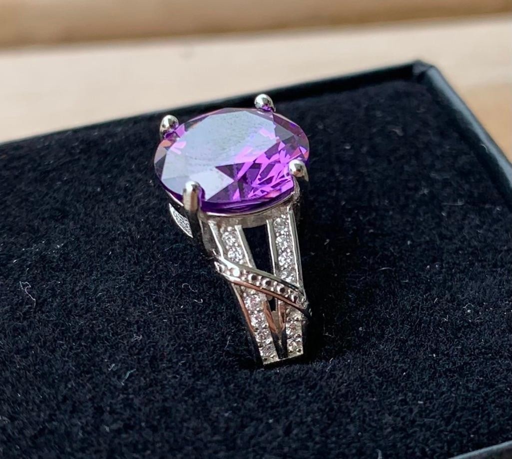 Sterling Silver Ring with Round Amethyst: Sterling Silver Ring with Round Amethyst This elegant sterling silver ring showcases a vibrant round-cut amethyst at its center, radiating a rich purple hue that catches the light beautifully. Subtle 