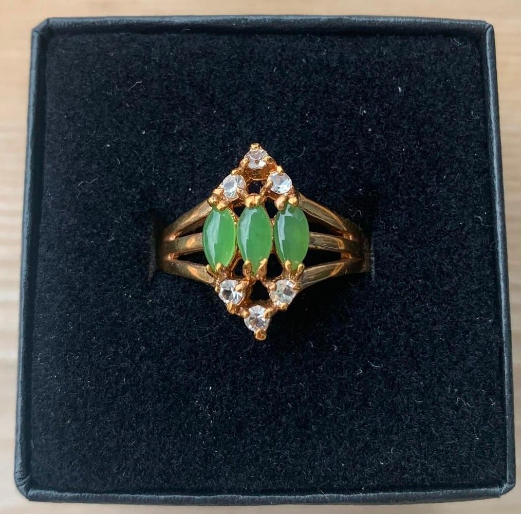 18kt Gold Electroplated Ring with Marquise Green Stones: 18kt Gold Electroplated Ring with Marquise Green Stones This elegant 18kt gold electroplated ring features three stunning marquise-cut green stones set prominently in the center. Complementing the vib