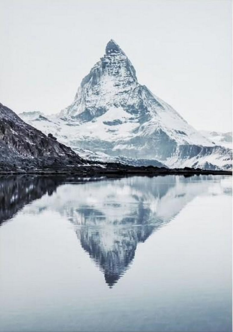 Alpine Reflection Canvas Print: Alpine Reflection Canvas Print An artwork showing a snow-capped mountain peak reflected in calm light blue water. The scene has a quiet and open atmosphere with clear, simple detail. The work is print