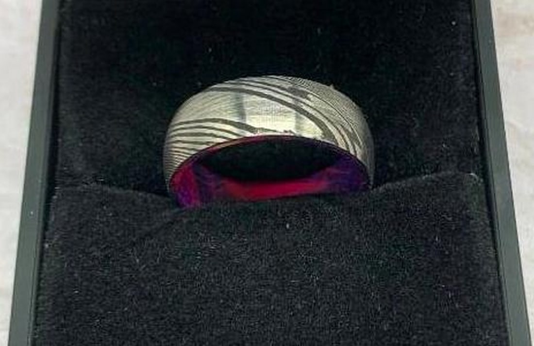 Damascus Steel Men's Ring with Pink & Blue Tie-Dye Inner Sleeve: Damascus Steel Men's Ring with Pink & Blue Tie-Dye Inner Sleeve This men's ring is a standout fusion of rugged craftsmanship and artistic flair. The exterior is crafted from black Damascus steel,