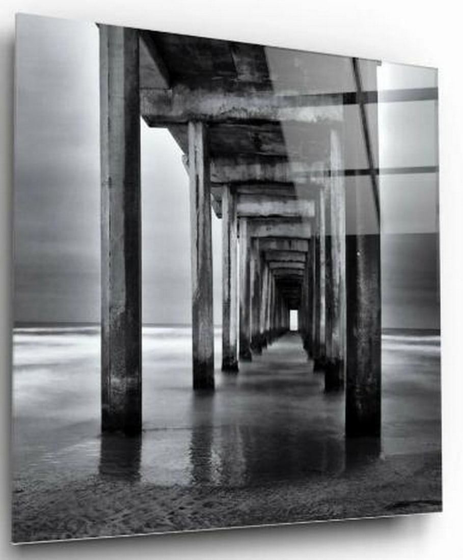 Beneath the Stillness Tempered Glass Wall Art: Beneath the Stillness Tempered Glass Wall Art This striking black and white tempered wall art captures a serene yet powerful perspective from beneath a weathered dock on a quiet beach. The play of lig