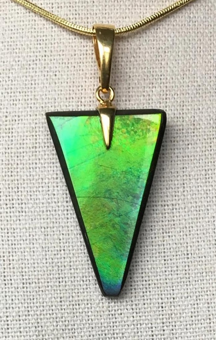 Prism Ammolite Necklace Pendant: Prism Ammolite Necklace Pendant This ammolite pendant showcases a beautifully cut designer gemstone, exuding elegance. The gem features a rich green hue with subtle gold and blue overtones, enhanced