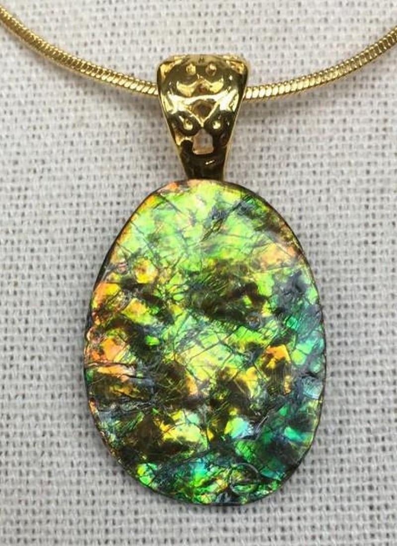 Iridescent Legacy Ammolite Pendant: Iridescent Legacy Ammolite Pendant This is an ammolite pendant with a green gemstone that has an uneven surface. There are some orange and gold toned highlights, along with some tiny hints of teal.