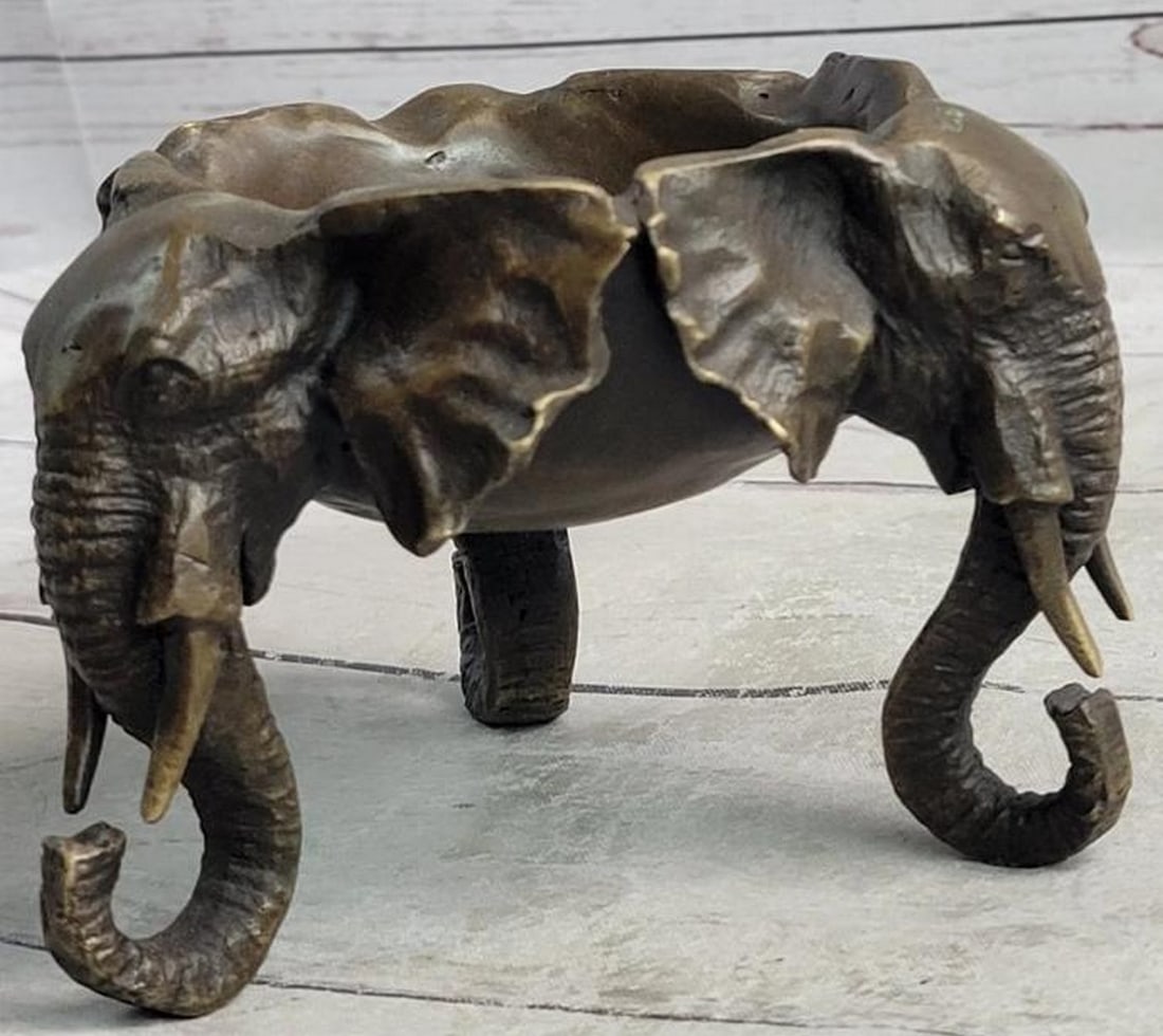 Trinity of Wisdom: Bronze Elephant Head Dish: Trinity of Wisdom: Bronze Elephant Head Dish A captivating fusion of form and function, this bronze sculpture dish features three intricately carved elephant heads encircling the sides. Each noble hea