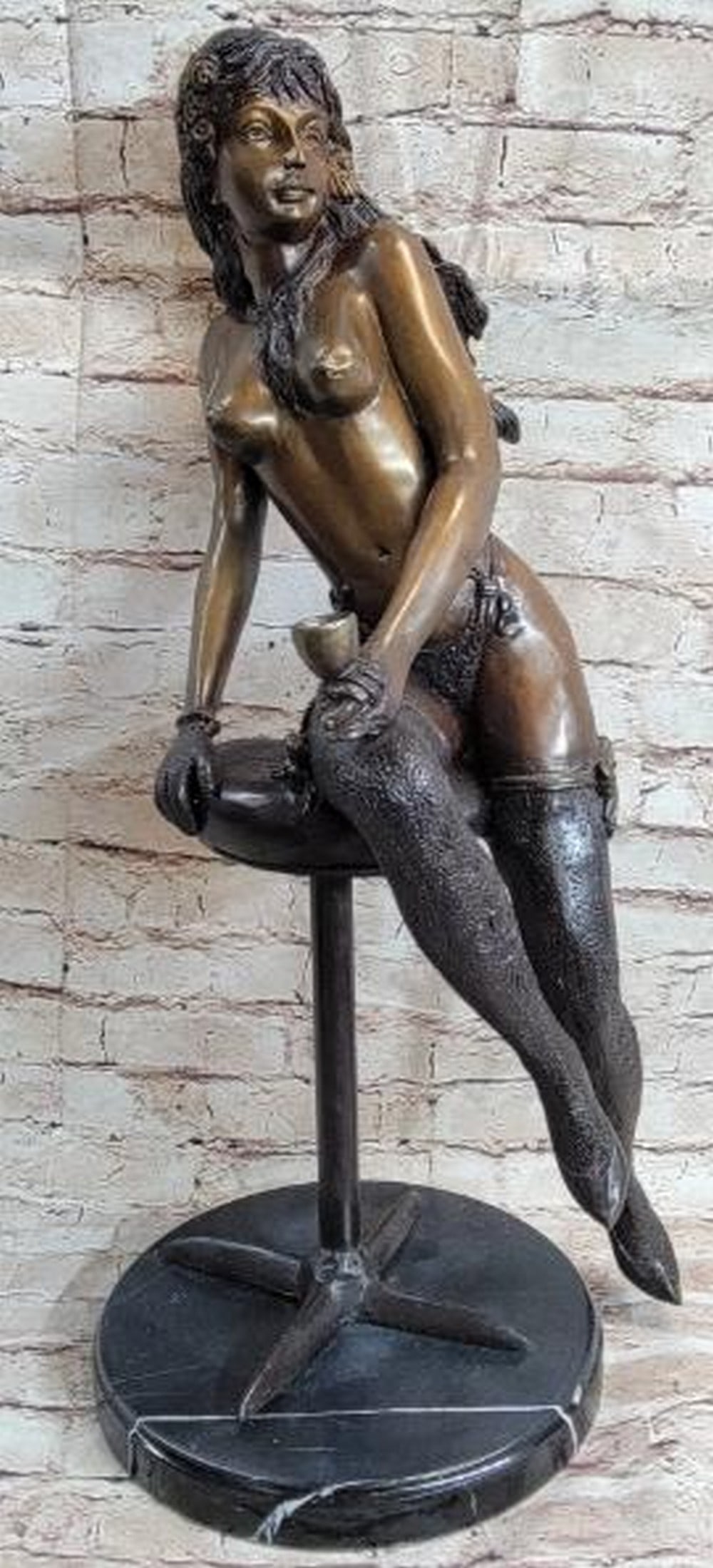 Nude Woman with Cup Bronze Sculpture: Nude Woman with Cup Bronze Sculpture This captivating bronze sculpture presents a moment of quiet allure and intimacy. A nude woman sits gracefully on a minimalist stool, holding a small cup as if pau