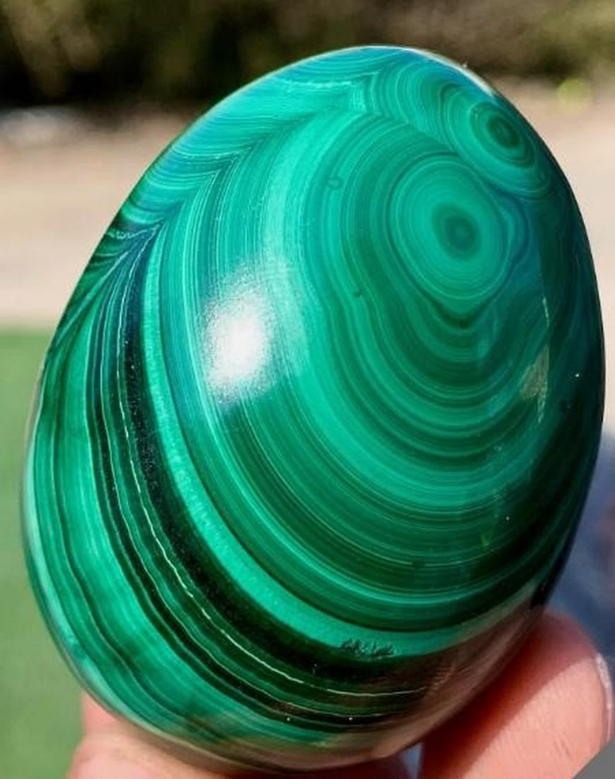 Malachite Egg with Transparent Crystalline Inclusions: Malachite Egg with Transparent Crystalline Inclusions This 175 gram natural malachite egg showcases deep forest-green banding and a lustrous, polished surface that highlights the stone's rich concentr