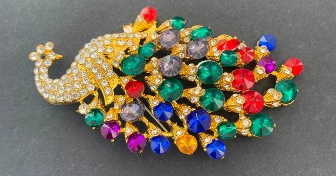 Radiant Gemstone Peacock Brooch: Radiant Gemstone Peacock Brooch A dazzling peacock brooch adorned with a vibrant array of colorful gemstones that shimmer across its elegantly detailed body. The head is crowned with brilliant silver