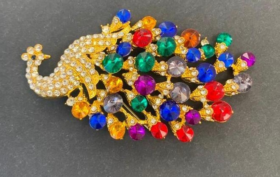 Radiant Gemstone Peacock Brooch: Radiant Gemstone Peacock Brooch A dazzling peacock brooch adorned with a vibrant array of colorful gemstones that shimmer across its elegantly detailed body. The head is crowned with brilliant silver