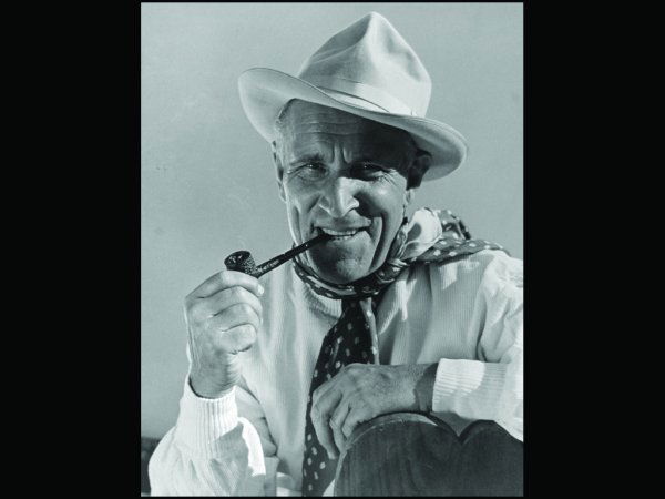 R85 - BLACK AND WHITE SILVER PRINT, 1930: Margaret Bourke-White print of a pipe-smoking man wearing a hat and scarf. The photo, taken in the USA, is matted and shrink wrapped. 12 x 14_