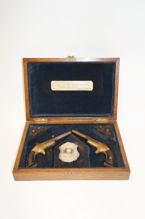 Suspender Pistols in Case and Badge: 32 Calibre rim fire Derringer pistols. Pair of suspender pistols of Alfred Y. Allee, Deputy Sheriff in Frio County, Texas. Included in the lot is Deputy Sheriff Allee's badge. Four bullets are in the