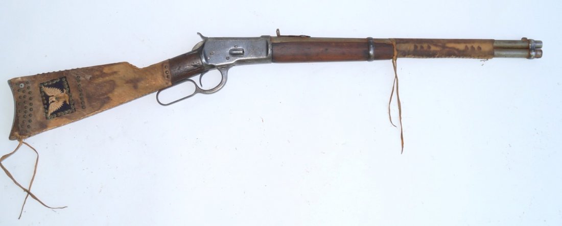 Winchester 1892 Saddle Ring Carbine: 44 W.C.F. Indian owned. Hide wrapped buttstock with brass tacks and stylized eagle on black felt background. Hide wrapped barrel and magazine 20" barrel. Bore average. Operating condition. Finish worn