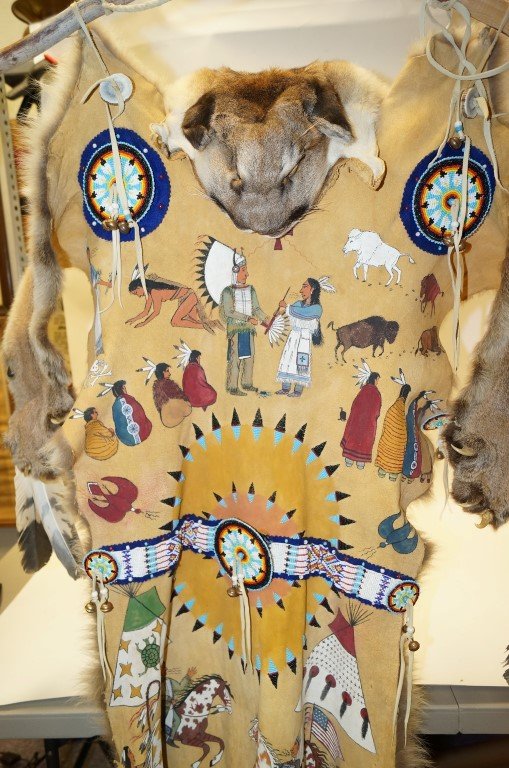 Bobcat Ceremonial Cloak: Bobcat fur on outside, beautifully painted hide decorated with beads, bells, and horn on the inside and at the edge. Scenes of Indian Chief, warriors riding horseback, carrying the American flag, teep