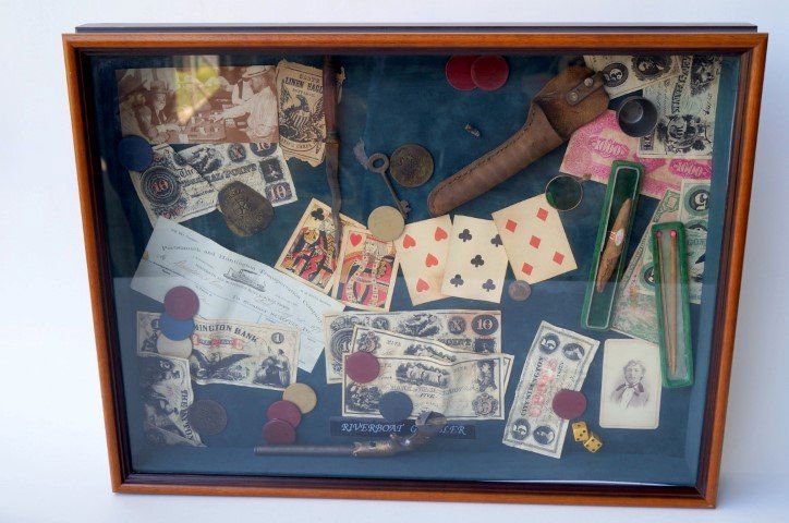 Riverboat Gambler's Display Box: Contains chips, money, a pistol, a dagger, a Marshall's badge of New Orleans, a cigar, a key, a photo, a monocle to detect marked cards, etc. 25" x 19".
