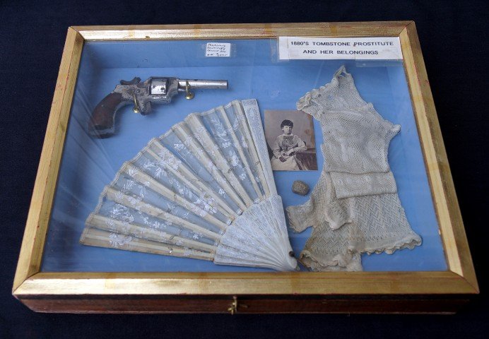 Tombstone Prostitute's Shadow Box: Properties of an 1880's Tombstone, Arizona prostitute. Arranged for display n a shadow box. Contains a ladies pistol; a lacy fan; two pairs wristlets; a photo and a silver nugget. 12" x 15"