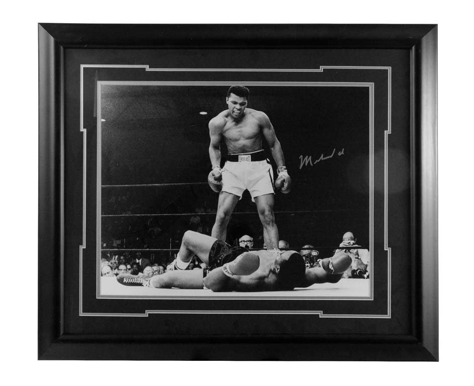 Autographed Photograph of Muhammad Ali defeating Sunny: Iconic photograph of a young Cassius Clay (Ali) looming over the fallen Sunny Liston in their legendary second fight. Taken by Neil Leifer. Autographed by Muhammad Ali. This includes a photograph of A