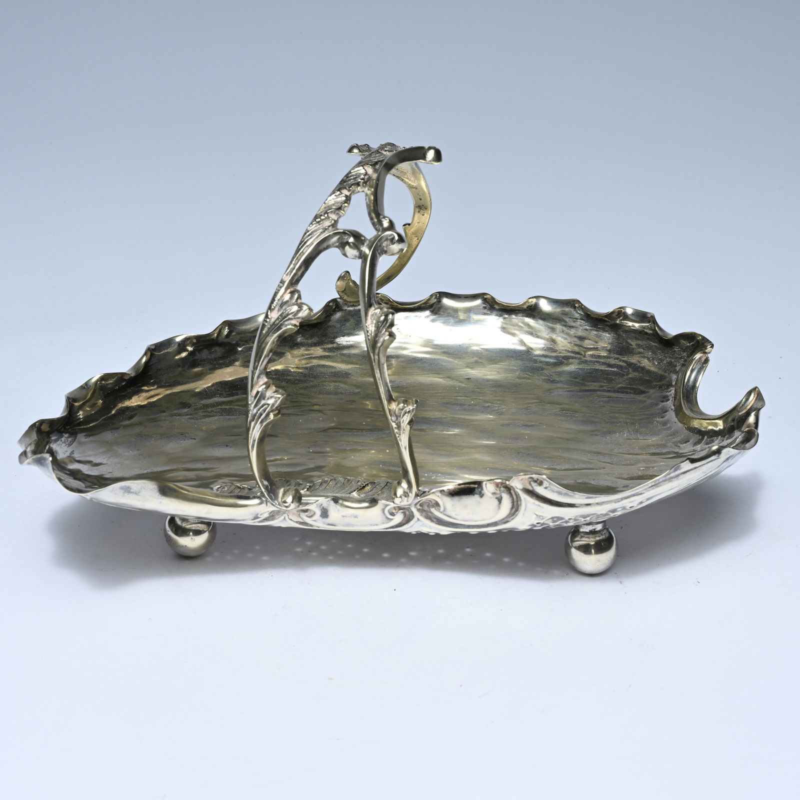 Art Nouveau dish, ca. 1900, on four legs, with a wavy edge and an elegant floral handle: Art Nouveau dish, ca. 1900, on four legs, with a wavy edge and an elegant floral handleArt Nouveau schotel, ca. 1900, op vier pootjes, met golvende rand en sierlijk florale greep12.5 x 13.5 x 24.5 cm