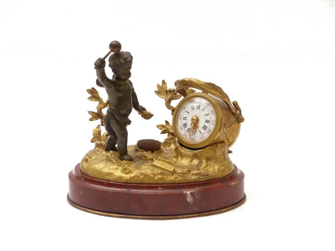 19th C. French Bronze & Marble Figural Clock: 19th C. French Bronze & Marble Figural Clock . France, 19th century Amor standing on a natural pedestal above an oval, profiled marble plinth with a quiver, swinging a mallet, small clock in the