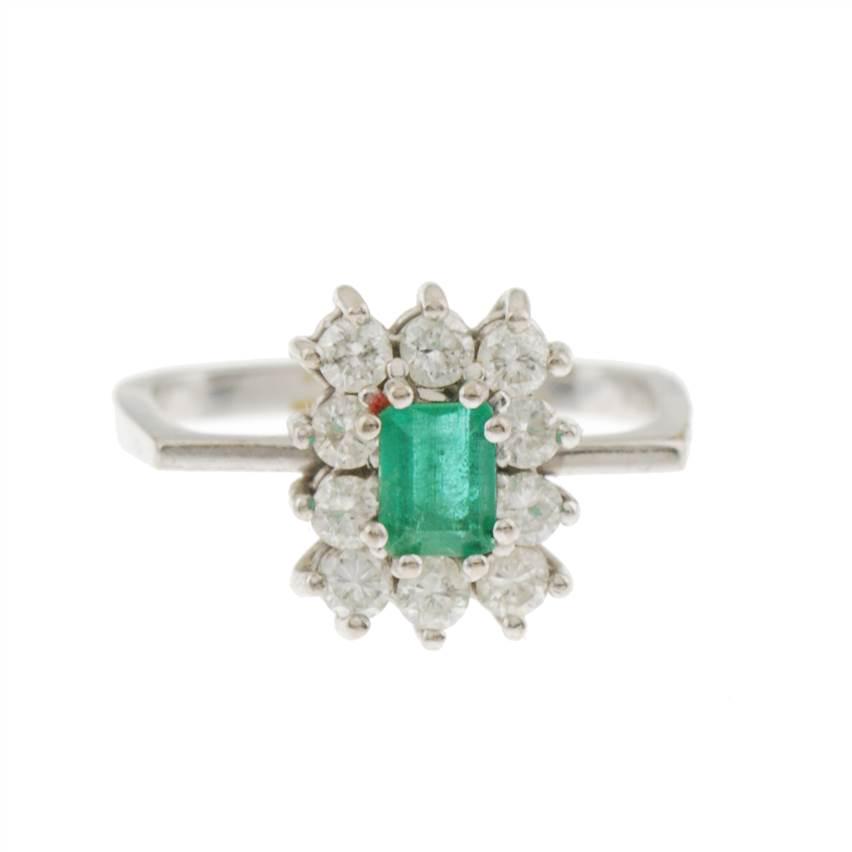 EMERALD AND DIAMOND ROSETTE RING.: White gold with emerald cut emerald, total weight approx. 0.4 ct. trimmed with brilliant cut diamonds, total weight approx. 0.50 ct. Band 17.5 mm. 4.6 gm.