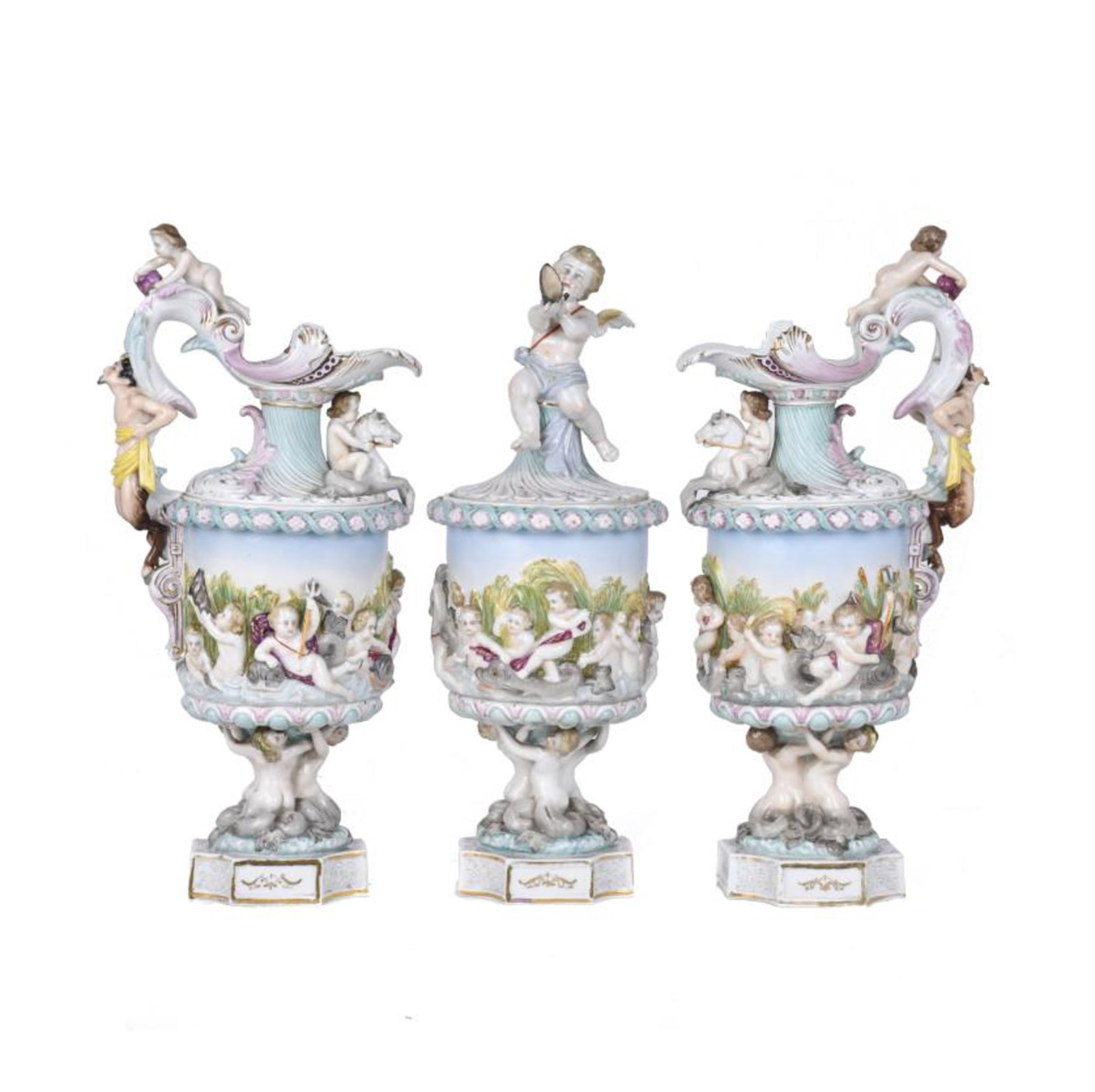 Pair of jugs and goblet in Capodimonte-style porcelain, 20th century.: Embossed enamelled porcelain with cherubs. Stamps on the base. With breaks and restorations. A wing from one of the cherubs is attached separately. Jugs: 38 x 18 x 13 cm; goblet: 37 x 14.5 cm diam.