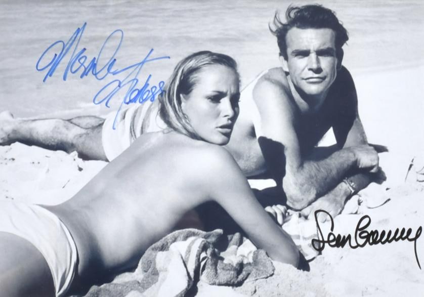 Bunny Yager (Pensilvania, 1929 - Florida, 2014). 'Dr. No'. Sean Connery and Ursula Andress, 1962.: Contemporary black and white print (circa 2018) Photograph autographed by Sean Connery (James Bond) and Ursula Andress (Honey). 20.4 x 29 cm; 35 x 41 cm (frame).