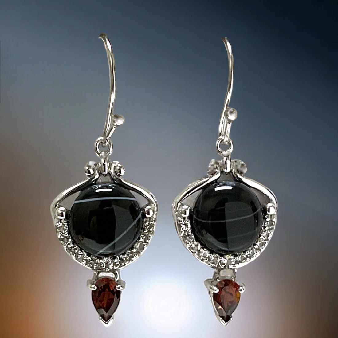 Shimmering Tuxedo Agate with a splash of Garnet makes these Sterling Silver Earrings a treasure: Product Details Item: Earrings Metal: Sterling Silver Gemstone: Tuxedo Agate & Garnet Approximate Measurements: 39.6 mm X 14.9 mm Ring Size: Not Applicable Chain Length: Not Applicable <